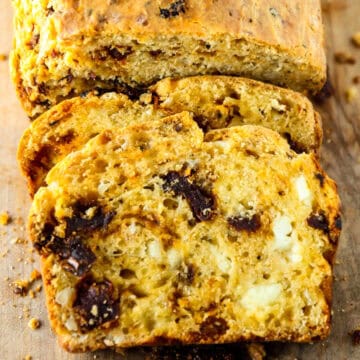 A loaf of sun-dried tomato bread with two slices cut.