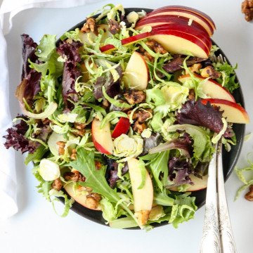 A top down view of shaved brussels sprouts and apple salad on a black plate with a fork.