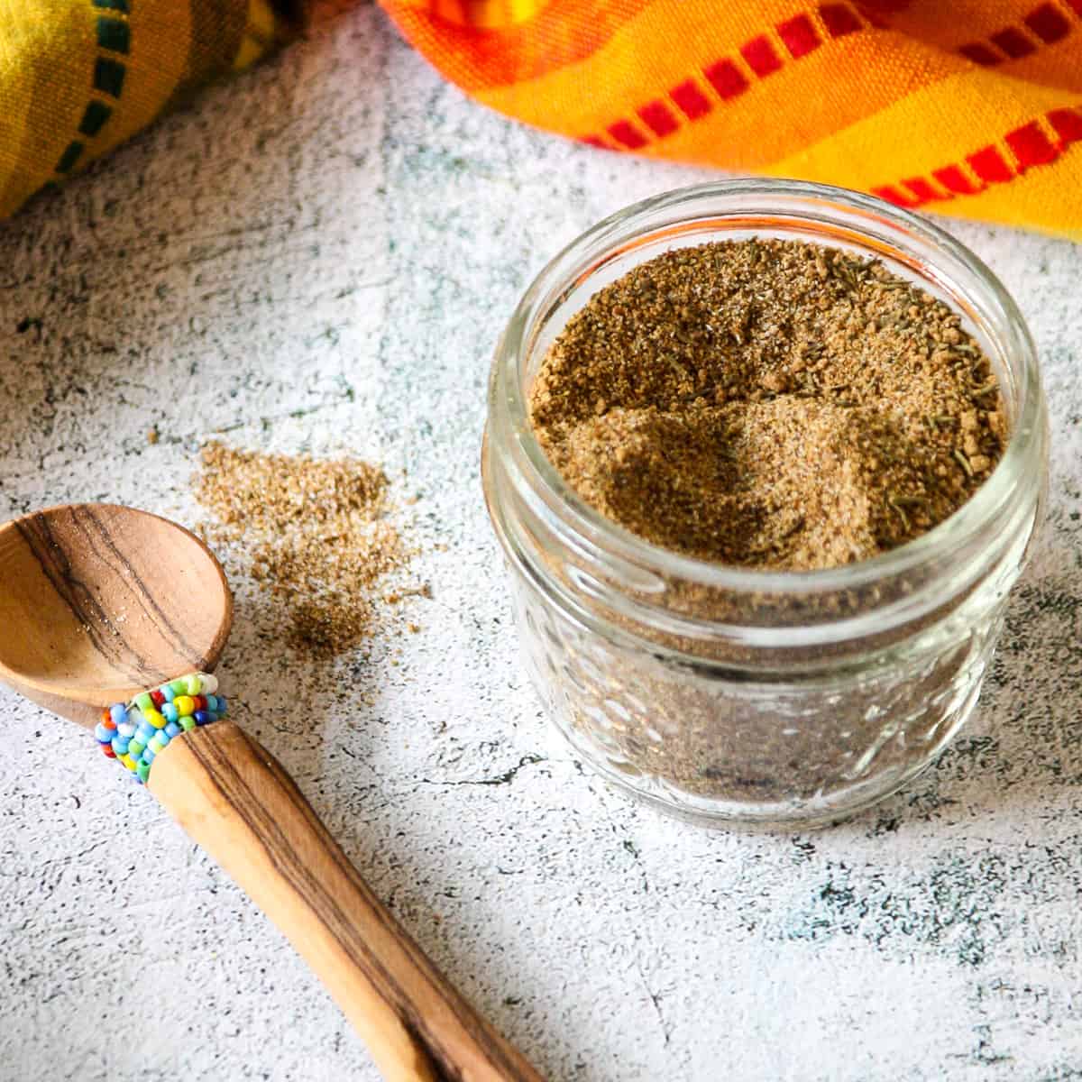 Jamaican jerk seasoning blend in a glass jar on a marble countertop.